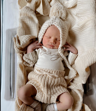 Baby photo of Darcy, the founder's child, wearing a hand-embroidered bodysuit in cream color.