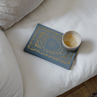 Blue book with gold text on a white surface next to a cup of coffee