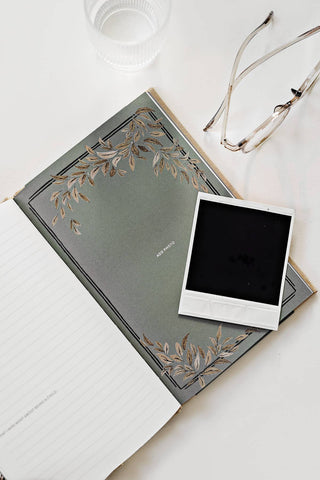 Gray notebook with floral design and a black square photo on a white surface