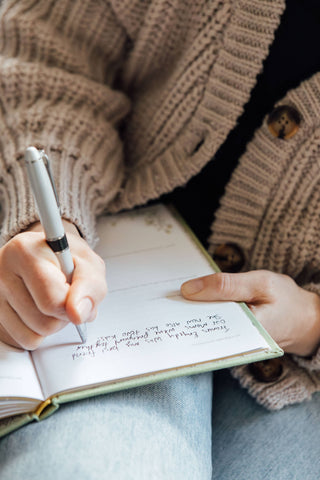 Person writing in a notebook with a pen, wearing a textured sweater.