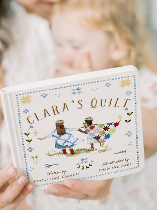 Book titled 'Clara's Quilt' held by a person with a blurred background