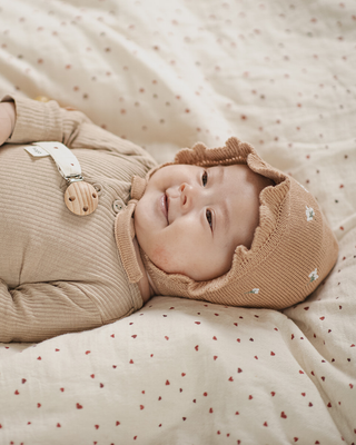 Baby wearing a brown knitted hat on a soft, patterned blanket