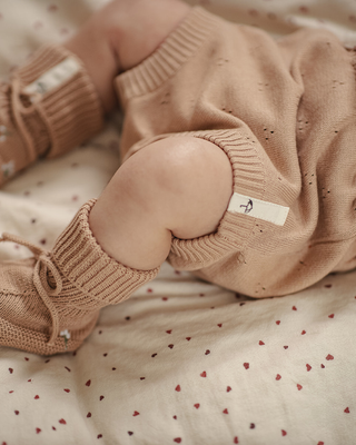 Close-up of a baby in a beige knitted outfit lying on a polka dot blanket.