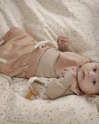 Baby lying on a polka dot blanket wearing a pink outfit.