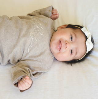 Baby with black hair wearing a neutral colored pullover with name embroidered on the front.