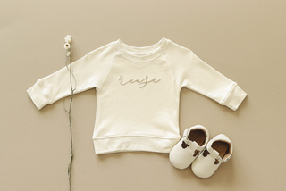 Cream colored child pullover with the name "Reese" embroidered in cursive in the center