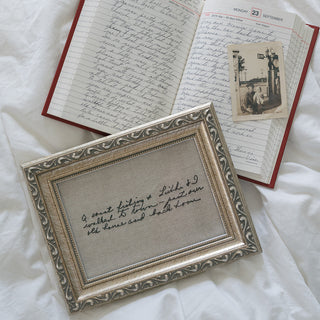 Open book with handwritten text and a framed letter on a white fabric background