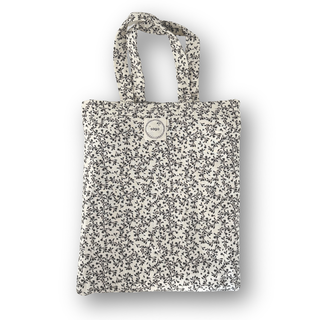 A reusable fabric tote bag with a dense black and gray floral print on a warm off-white background, featuring two top handles and a circular metal logo plate on the front. The brand name 'sage' is visible on the plate.