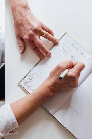 Person writing in a notebook with a pen on a white surface